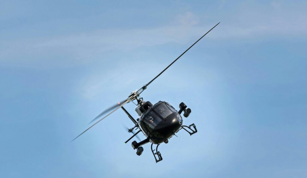 A black helicopter captured mid-flight in a clear blue sky, showcasing its dynamic presence and motion.